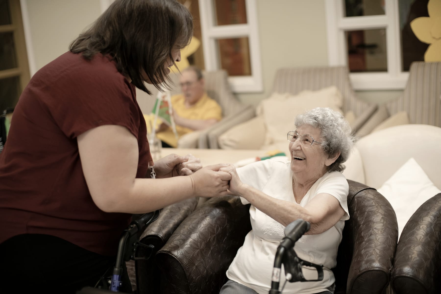 A caregiver holds hands with a laughing older woman
