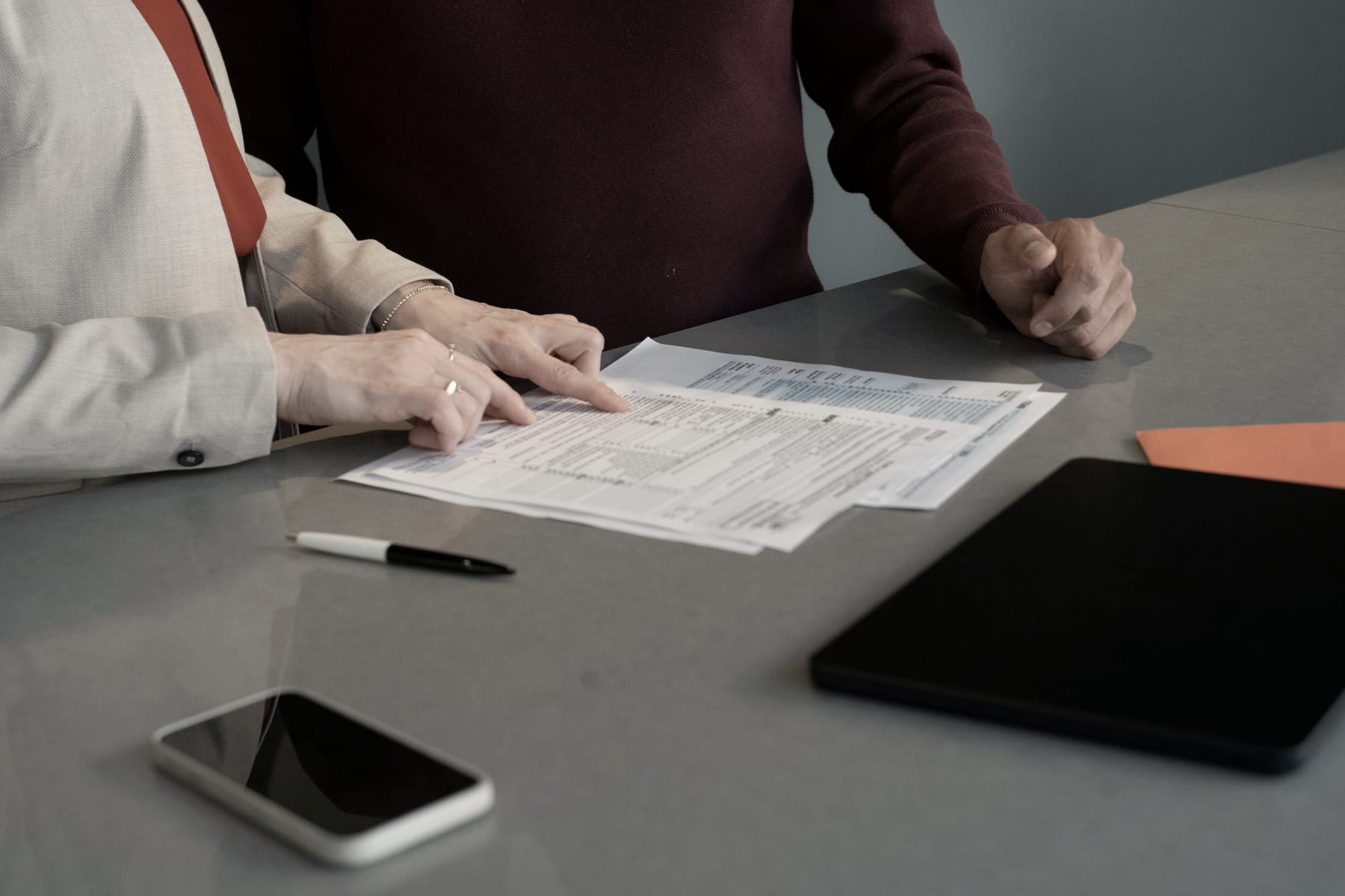 Two people go through printed forms at a desk